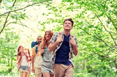 adventure, travel, tourism, hike and people concept - group of smiling friends walking with backpacks in woods