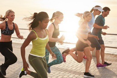 portrait of healthy young men and women running race on seaside promenade. group of young people sprinting outdoors at sunset.
