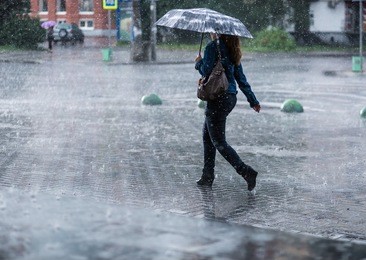 woman with umbrella going on street during heavy rain .