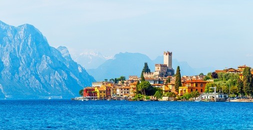 ancient tower and fortress in old town malcesine at garda lake veneto region italy high snowbound top mountains on background summer landscape with colorful houses green trees