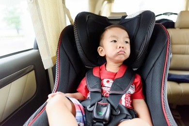 asian boy wearing red t-shirt in safety car seat. unhappy child.