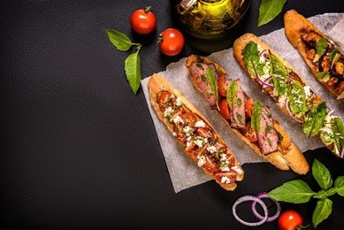 various bruschettas on a black background with olive oil, tomatoes, and fresh basil leaves. top view. free space for text.