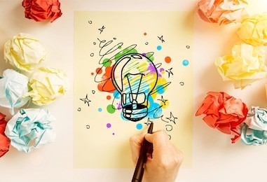 creative idea concept with hand drawing abstract lightbulb sketch on paper sheet surrounded with colorful crumpled paper balls