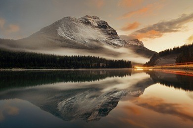 mountain lake and traffic light trail with reflection and fog at sunset in banff national park, canada.
