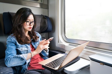 cute asian woman using smartphone and laptop on train, copy space on window, business travel or technology concept