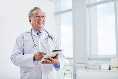 aged asian doctor using digital tablet in clinic