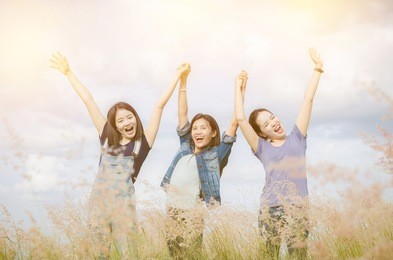 three happy asian girls smiling and staying in raised hands at grass field with vintage filter, happiness and togetherness concept.
