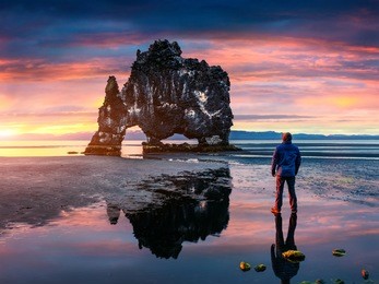 man stands on the surface of water at fall of tide and and admiring of sunrise. huge basalt stack hvitserkur on the eastern shore of the vatnsnes peninsula, iceland, europe. 