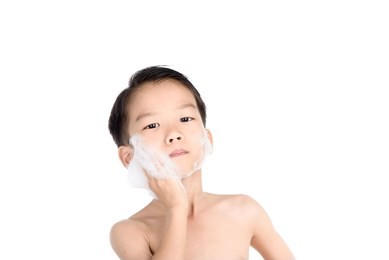 young boy put foam on his face before shaving in the bathroom.
