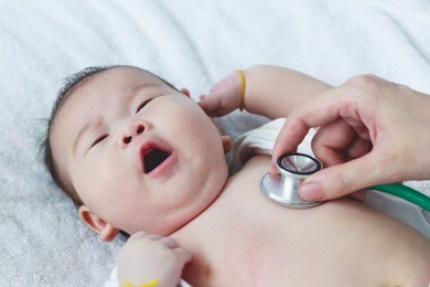 professional pediatrician examining infant. doctor using a stethoscope to listen to kid's chest checking heartbeat. two months baby asian girl lying on sickbed in hospital.