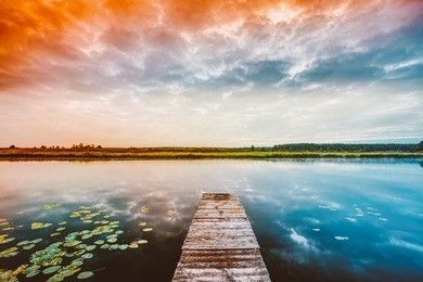 wooden boards pier on calm water of lake, river at sunset time, forest on other side. landscape. nature background.
