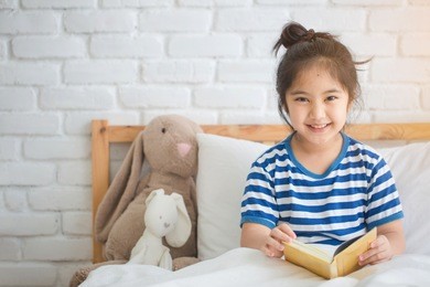 happy asian girl reading story book on the bed