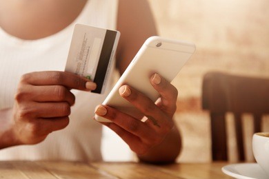 people and technology concept. cropped portrait of young woman wearing white top holding credit card, transferring money from her account via online banking application using mobile phone. film effect