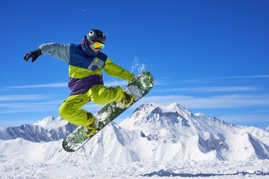 snowboarder in bright sportswear doing trick against of beautiful mountains