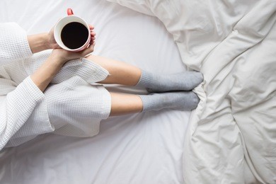 young woman drinking her coffee while sitting on bed. lazy sunny morning in bed