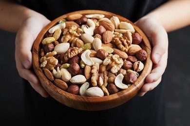 children hands holding a wooden bowl with mixed nuts. healthy food and snack. walnut, pistachios, almonds, hazelnuts and cashews.