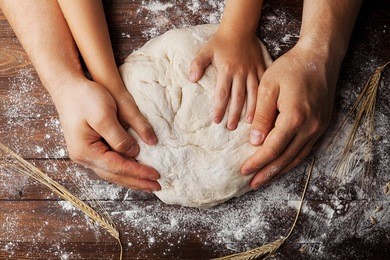 father and child hands prepares the dough with flour, rolling pin and wheat ears on rustic wooden table from above. homemade pastry for bread or pizza. bakery background.