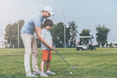 sharing golf experience. cheerful young man teaching his son to play golf while standing on the golf course