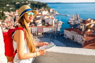 young female traveler with red backpack and hat enjoying the view from george's tower on piran old town. traveling in slovenia