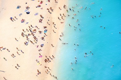 people bathing in the sun, swiming and playing games on the beach. tourists on the sand beach of navagio zakynthos greece.