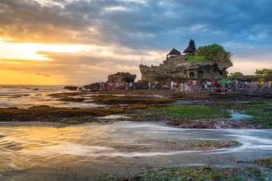 tourist crowd walk into the see to pura tanah lot , hindu temple that is one of the most favourite dramatic sunsets scene of bali.