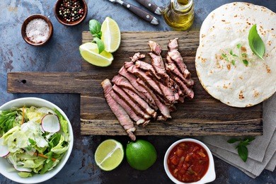cooking steak tacos with sliced meet and tortillas on a cutting board