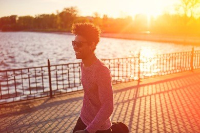 happy afro american teenage man walking on promenade. curly young black male hipster on autumn day. direct sunlight and warm filter effect.