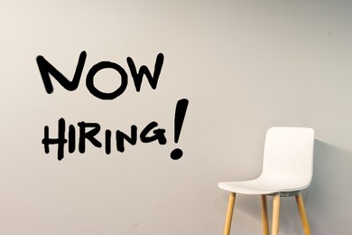 job recruiting advertisement represented by 'now hiring' texts on the  wall. the single chair is used to represent the hiring position to be recruited and filled.