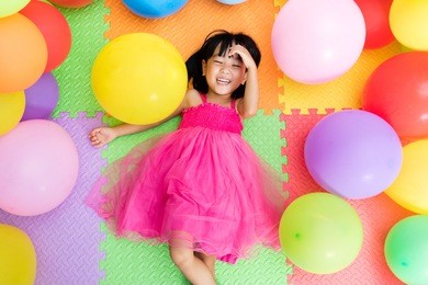 asian little chinese girl lying on the floor amongst colorful balloons in indoor playground