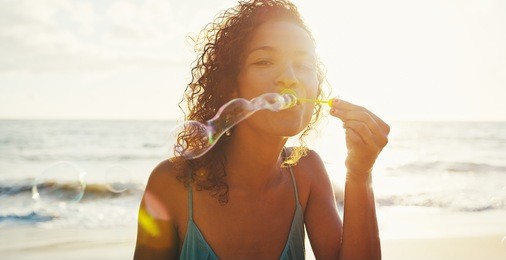 happy young woman blowing bubbles on the beach at sunset