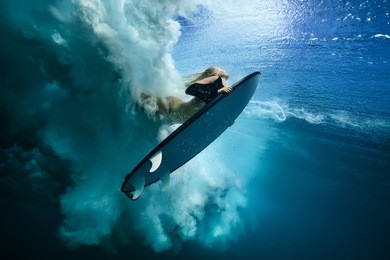 beautiful surfer diving duckdive under big ocean wave. turbulent air bubbles and tracks after sea wave crashing. ripples at water surface with sky color.