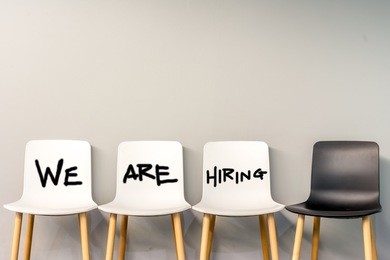 job recruiting advertisement represented by 'we are hiring' texts on the chairs or wall. one chair is colored differently to represent the hiring position to be recruited and filled.