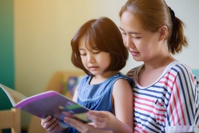 happy asian girl reading story book with her mother together
