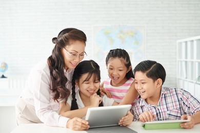 pupils and their mature teacher watching something on tablet