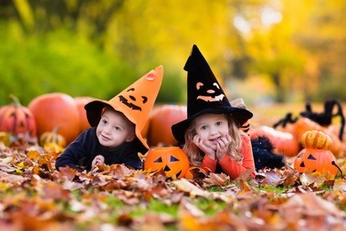 children wearing black and orange witch costumes with hats playing with pumpkin and spider in autumn park on halloween. kids trick or treat. boy and girl carving pumpkins.