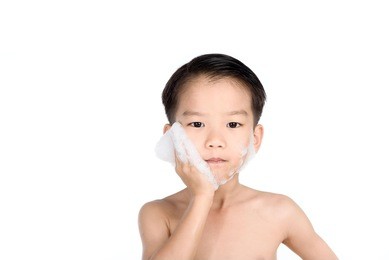 young boy put foam on his face before shaving in the bathroom.