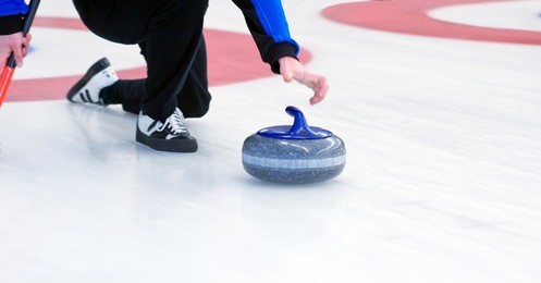 curling player delivering a stone on a curling rink, sliding over the ice