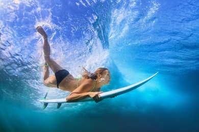 adult active girl in bikini in action - surfer with surf board dive underwater under breaking big ocean wave. family lifestyle, people water sport adventure camp, beach extreme swim on summer vacation