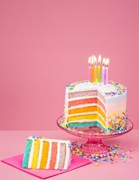 colorful rainbow birthday cake with candles over a pink background.