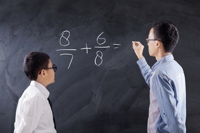 photo of a young man teaches equations formula on the little boy while writing on the blackboard, shot in the class