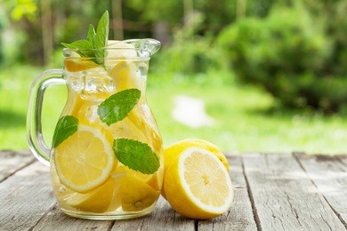 lemonade pitcher with lemon, mint and ice on garden table. view with copy space