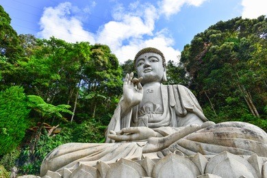 a buddha statue overlooks a valley through the trees and the mist at the chin swee caves in malaysia in the genting highlands.