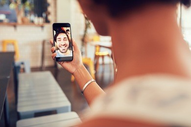 man and woman talking to each other through a videochat on a mobile phone. woman having a video call with man on her smart phone. woman sitting at a coffee shop.