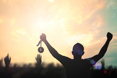 winner concept: silhouette champion hand holding gold medal reward against blurred sport stadium sunset background