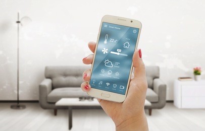 home temperature, safety and environment control on mobile app. smart phone in woman hand. living room in background.