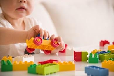 close up of child's hands playing with colorful plastic bricks at the table. toddler having fun and building out of bright constructor bricks. early learning.  stripe background. developing toys