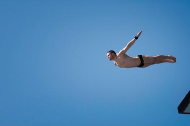 young man swan diving from 10 meter high platform