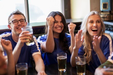 sport, people, leisure, friendship and entertainment concept - happy football fans or friends with beer watching game and celebrating victory at bar or pub