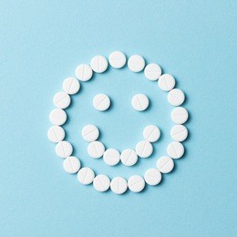 smiling face made from white round pills on blue background