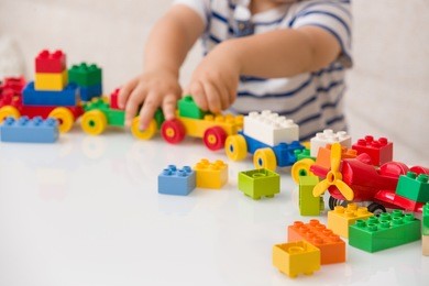 close up of child's hands playing with colorful plastic bricks at the table. toddler having fun and building out of bright constructor bricks. early learning.  stripe background. developing toys